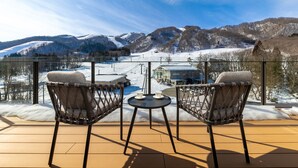 Un balcon avec deux fauteuils en osier et une petite table, donnant sur un paysage montagneux enneigé.