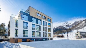 Un bâtiment moderne à plusieurs étages, doté de grandes fenêtres et d’un toit plat, entouré de neige et de montagnes.