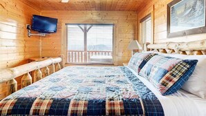 A wooden cabin room with a bed, a mounted TV, and a window with a balcony. - Majestic Smoky Mountains Views | HotTub (Sevierville)