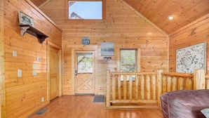 A cabin interior with wooden walls, a wooden bench, a door with a cross pattern, and a small window. - Majestic Smoky Mountains Views | HotTub (Sevierville)