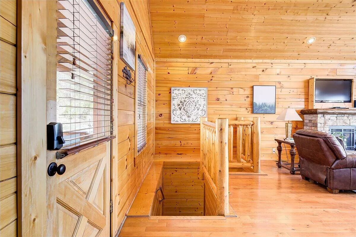 A wooden interior with a fireplace, a TV, and a staircase leading to a lower level.