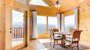 A wooden cabin with a dining area, large windows, and a balcony. - Majestic Smoky Mountains Views | HotTub (Sevierville)