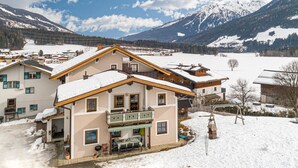A snow-covered chalet with a balcony, surrounded by a snowy landscape and mountains.