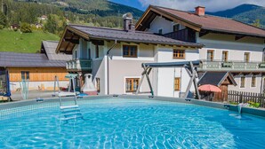 A swimming pool with clear blue water, surrounded by a building with a sloped roof and wooden exterior.