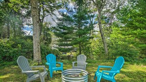 A circular seating area with a metal fire pit surrounded by four Adirondack chairs in different colors. - Coastal Comfort Near the Bay! 'Buttermilk Cottage' (Wareham)