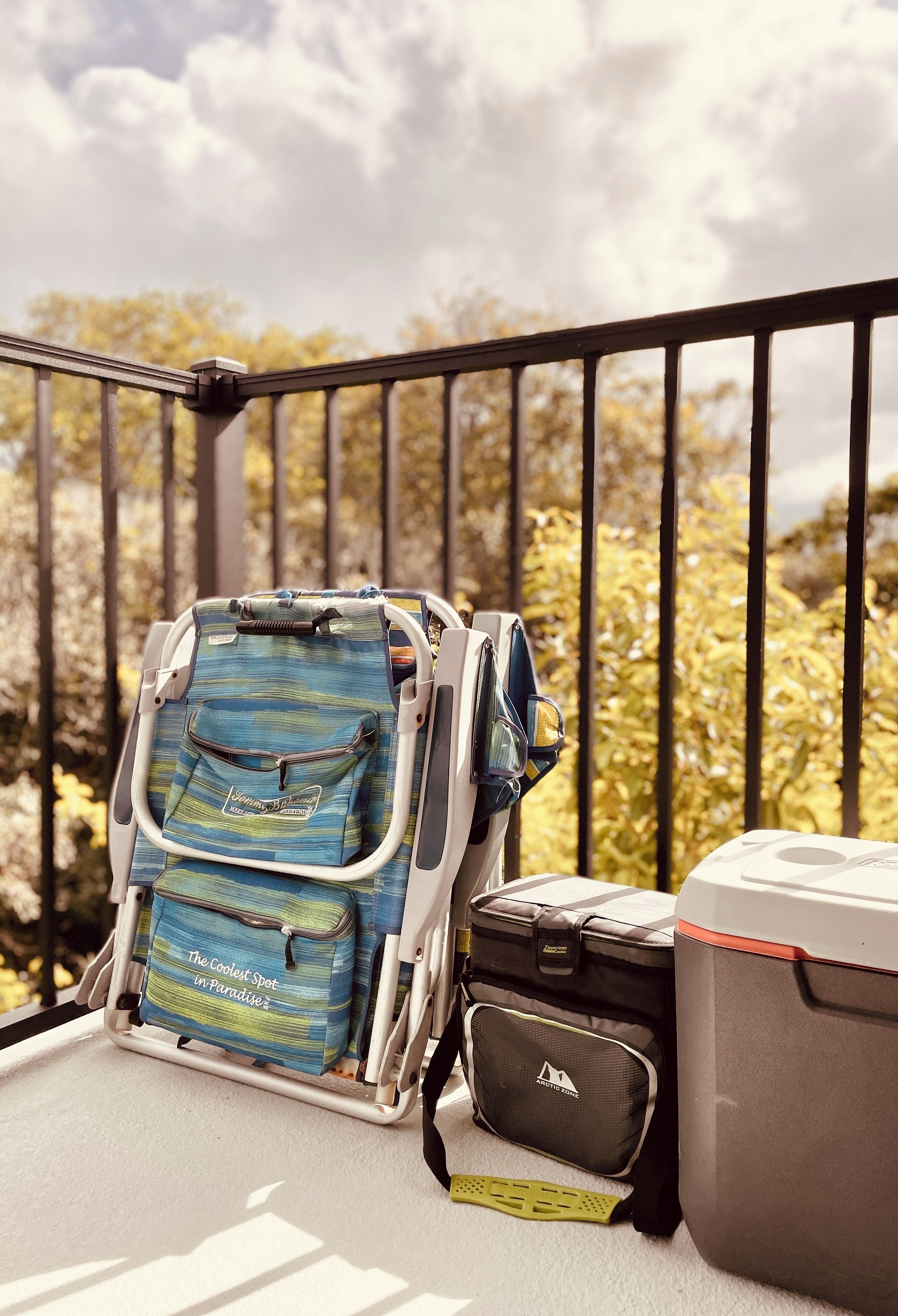 Un balcon avec une chaise, une glacière et un sac.