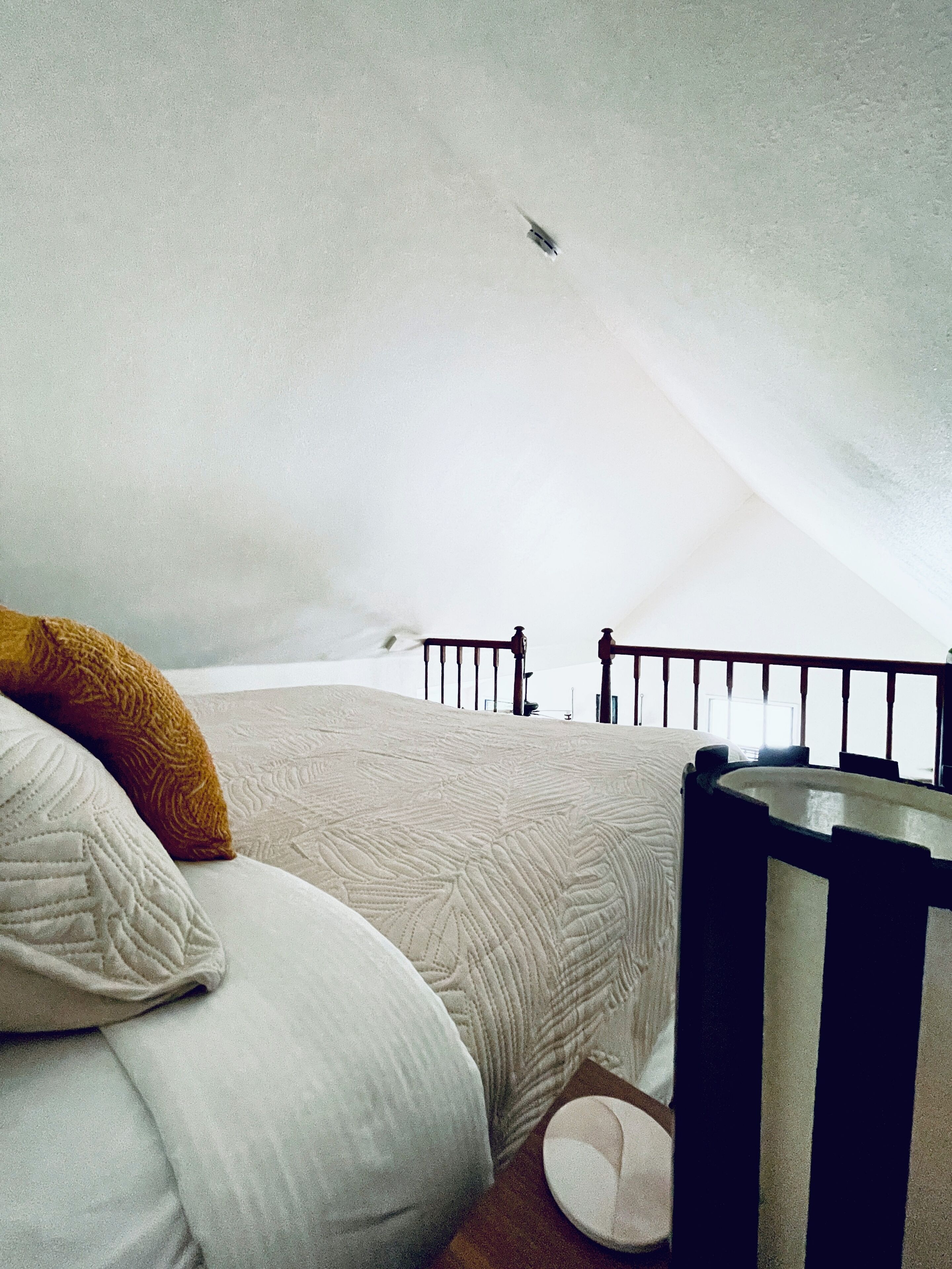 A bedroom with a bed, pillows, a crib, and a view of the sky.