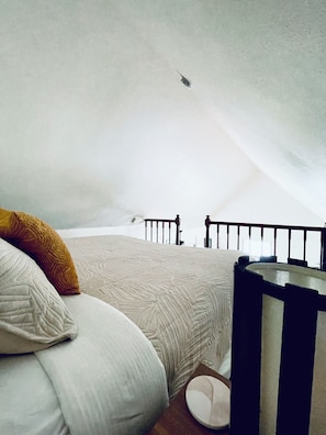 A bedroom with a bed, pillows, a crib, and a view of the sky. - Elegant Princeville Condo with Cozy Loft Bedroom and Mountain Views (Princeville)