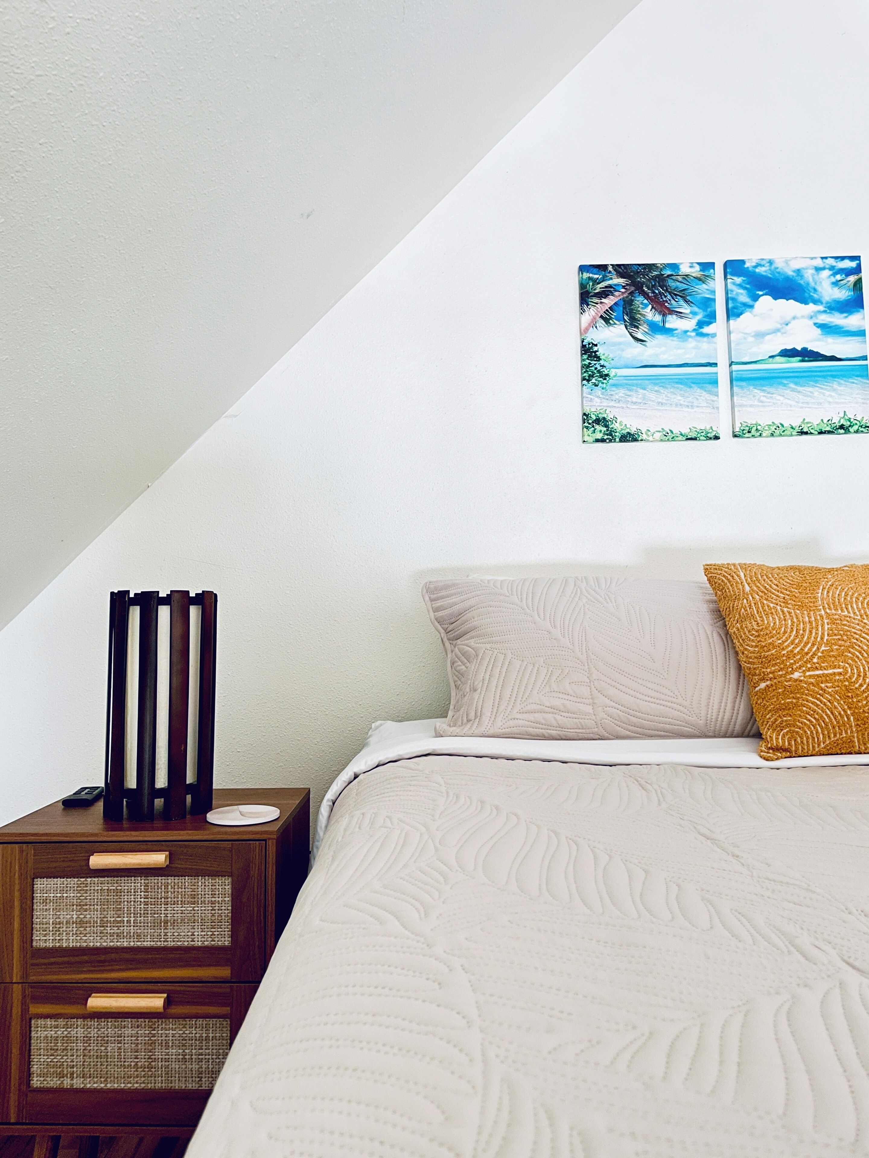 Un dormitorio con cama, mesita de noche, un cuadro en la pared y una mesita de noche de madera con cajones.