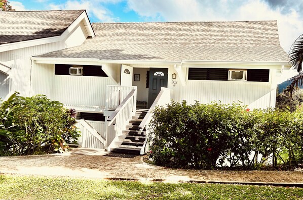 A white house with a front porch, a staircase, and a number "202" on the door. - Elegant Princeville Condo with Cozy Loft Bedroom and Mountain Views (Princeville)