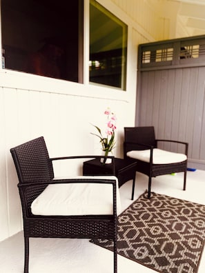 A patio area with two wicker chairs and a small table, a patterned rug, and a potted plant. - Elegant Princeville Condo with Cozy Loft Bedroom and Mountain Views (Princeville)