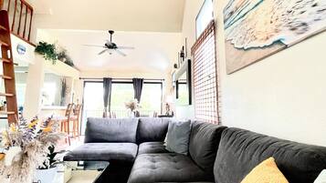 A living room with a sectional sofa, a ceiling fan, a dining area with chairs, and a painting on the wall.