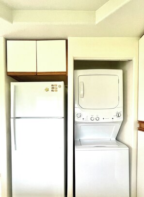 A compact kitchen with a refrigerator and a built-in washer and dryer. - Elegant Princeville Condo with Cozy Loft Bedroom and Mountain Views (Princeville)