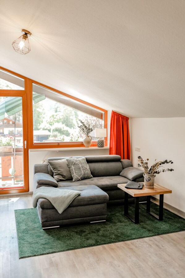 A modern living room with a grey sectional sofa, a wooden coffee table, and a green rug.