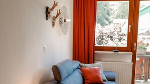 A cozy living room with a blue sofa, a small wooden table, and a window with red curtains.