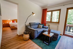 Une pièce moderne avec un canapé gris, une petite table, une lampe et une fenêtre avec des rideaux.