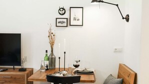 A modern living room with a wooden table, a black chair, a wooden bench, and a TV on a wooden stand. - Vacation apartment Kehlstein 2 persons, 40 sqm (Schönau am Königssee)