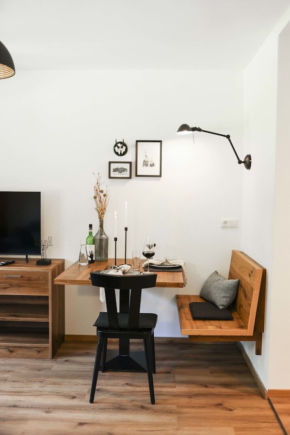 Un salon moderne avec une table en bois, une chaise noire, un banc en bois et un téléviseur posé sur un meuble en bois.