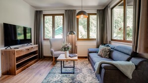 Una sala de estar moderna con televisor, sofá, sillón y una mesa con lámpara.