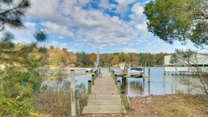 A wooden dock leading to a docked boat, surrounded by trees and a body of water.