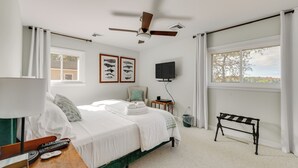 A bedroom with a bed, a ceiling fan, a TV, a window, and a small table.