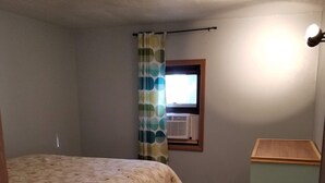 Une chambre à coucher avec un lit, une fenêtre avec des rideaux, un radiateur et un petit meuble.