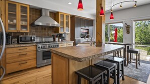Une cuisine moderne dotée de plans de travail en granit, d’appareils électroménagers en acier inoxydable, d’armoires en bois et d’un grand îlot central avec des tabourets de bar.