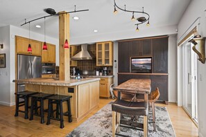 Una cocina moderna con armarios de madera, electrodomésticos de acero inoxidable, una isla central con taburetes, iluminación colgante y un ventanal con vistas.