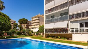 Una piscina con agua cristalina azul, rodeada por un césped cuidado y un edificio con balcones.