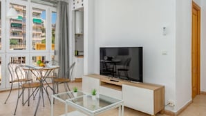 Una sala moderna con una mesa de centro de vidrio, un televisor sobre un mueble de madera, y una zona de comedor con sillas y una mesa.