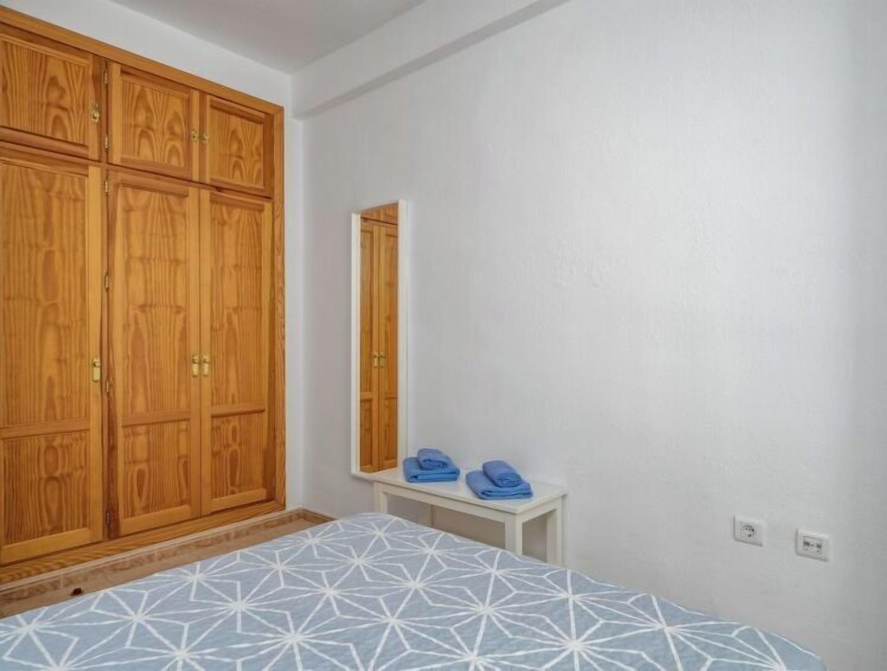 Une chambre à coucher avec un lit, une armoire, un miroir et une petite table sur laquelle sont pliées des serviettes.