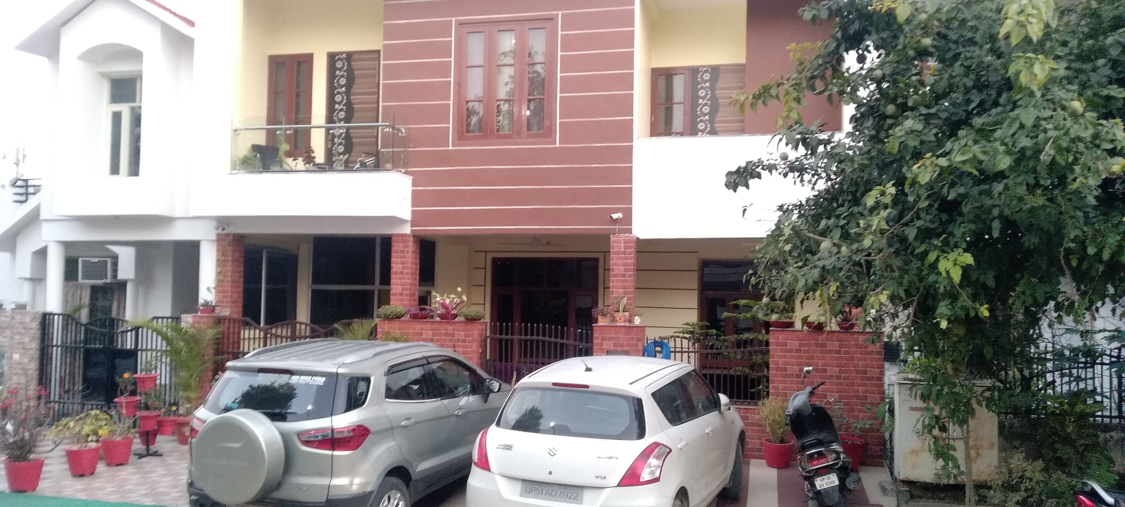 A two-story house with a balcony, a garage, and a driveway with two cars parked.