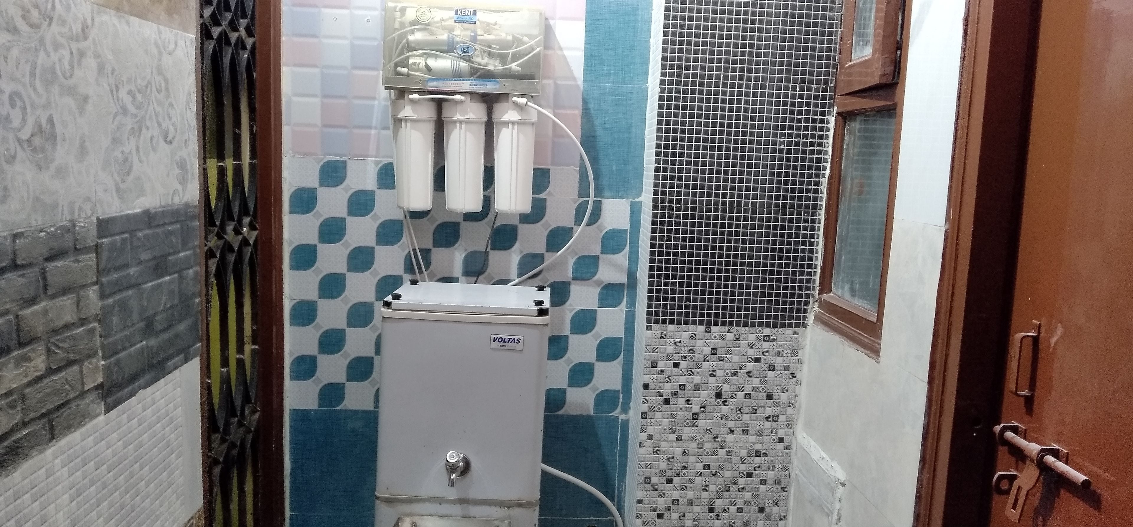 Casa de banho com sistema de filtragem de água, parede revestida com padrão azul e branco, e porta de metal.