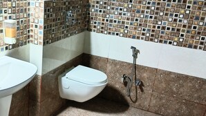 Ein Badezimmer mit einem weißen Waschbecken, einer Toilette und einer Dusche. Die Wände sind mit einem Mosaikmuster gefliest.