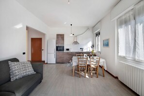 Une cuisine moderne équipée d’un four à micro-ondes, d’une cuisinière et d’une hotte aspirante. On y trouve une table à manger avec des chaises, ainsi qu’un canapé agrément é d’un coussin à motifs.