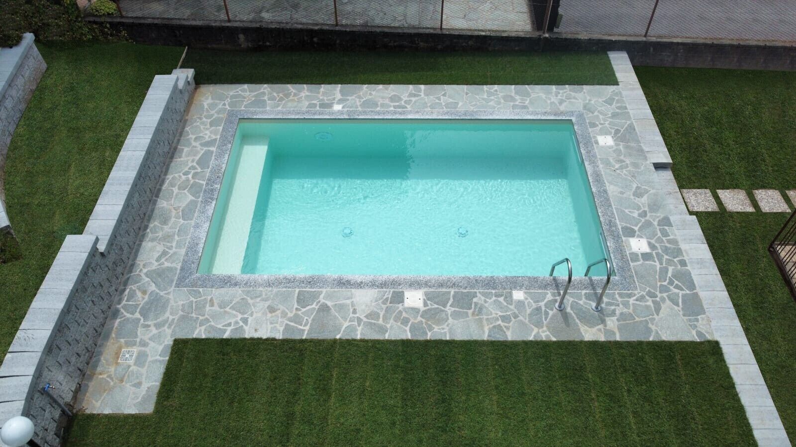 Una piscina rettangolare con piastrelle in pietra e un'area circostante erbosa.