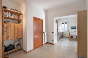 Une pièce avec des meubles de rangement en bois, un radiateur, une table à manger avec des chaises et un coin cuisine avec une fenêtre.