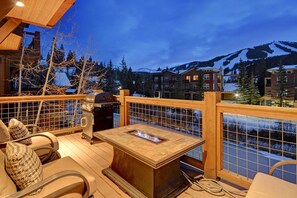 Un patio in legno con un braciere, posti a sedere all'aperto e vista sulle montagne innevate.