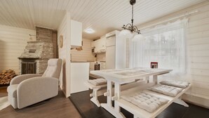 Un interior de cabaña acogedor con chimenea, una mesa de comedor con bancos y una zona de cocina.
