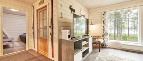 A cozy cabin interior with a wooden interior, a television on a stand, a sofa, and a window with a view of trees.