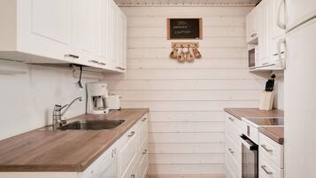 A compact kitchen with white cabinetry, a wooden countertop, a coffee maker, and a chalkboard sign.
