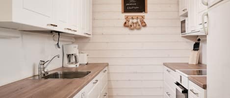 A compact kitchen with white cabinetry, a wooden countertop, a coffee maker, and a chalkboard sign.