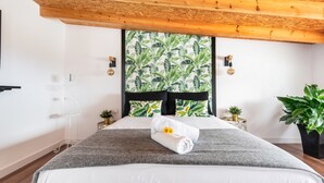 A neatly made bed with a rolled towel and a flower, a window with a tropical leaf pattern, and a wooden ceiling. - Holiday Home "Casa Adayeim 2" with Mountain and Sea Views (ICOD DE LOS VINOS)