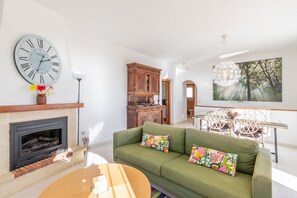 A living room with a green sofa, a fireplace, a wooden cabinet, and a large clock.