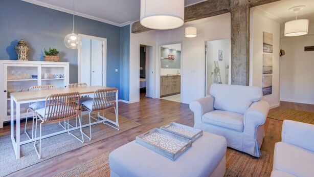 Un salon moderne avec un coin repas, des meubles blancs et une cuisine en arrière-plan.