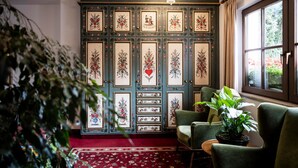 Una habitación con pared estampada, alfombra roja, sillón verde y ventana con cortinas.