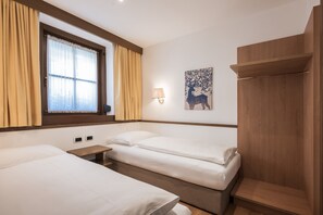 Una habitación de hotel con dos camas individuales, un armario de madera, una ventana con cortinas y una lámpara fijada a la pared.