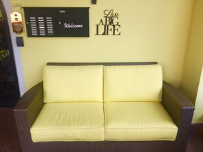 A yellow sofa with a woven frame, a wall-mounted intercom, and a 'Live ABG LIFE' sign.