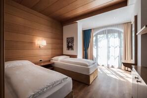 A hotel room with two beds, wooden panel walls, a painting, a window with curtains, and a bedside table.
