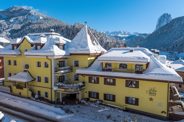 A yellow building with a balcony, a sign reading 'Stella Residence,' and snow-covered surroundings.